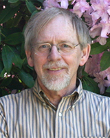 A Caucasian man with a goatee, wearing glasses and a striped shirt, with blonde hair.